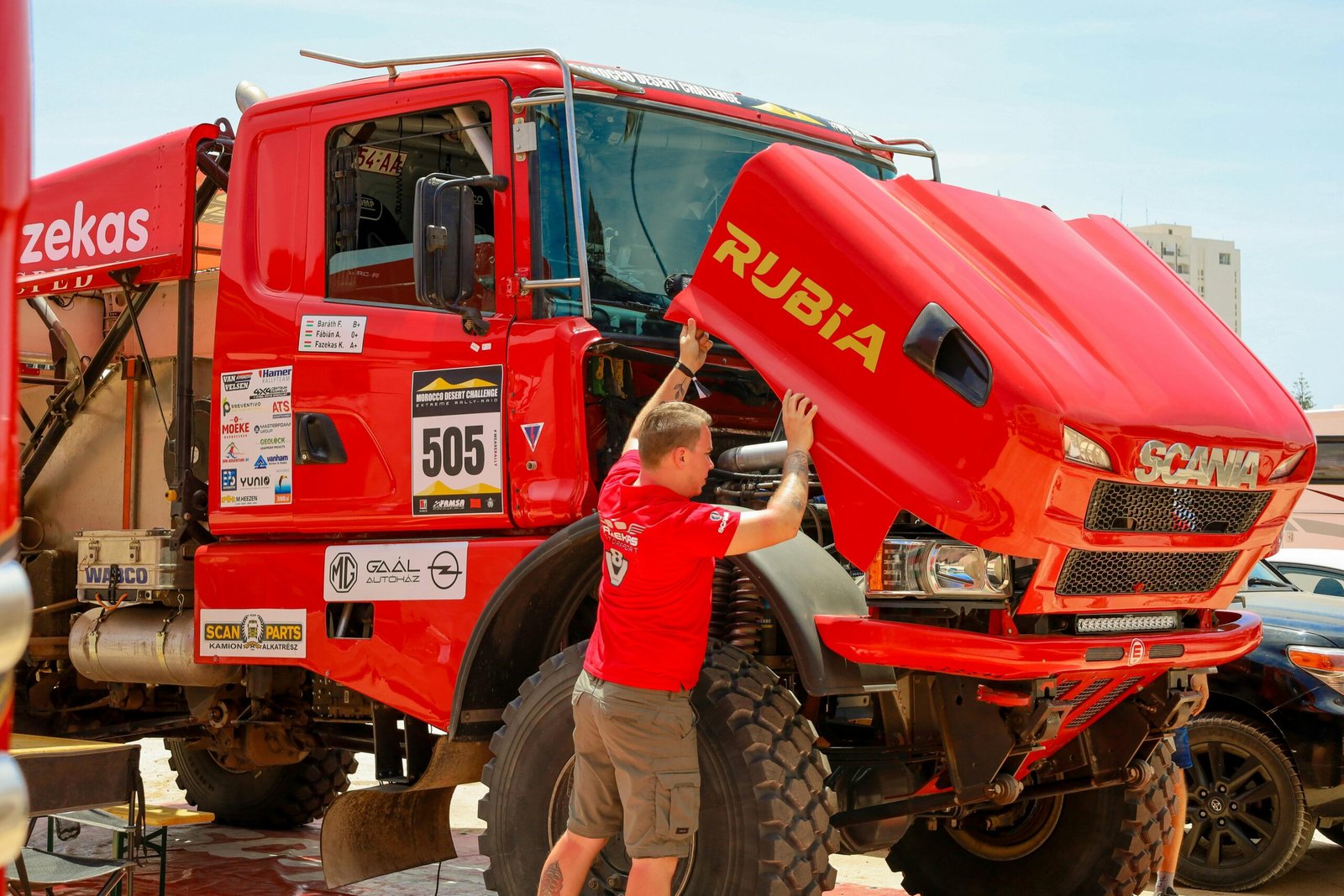 Mechanic checking a red rally truck's engine during a desert competition event.